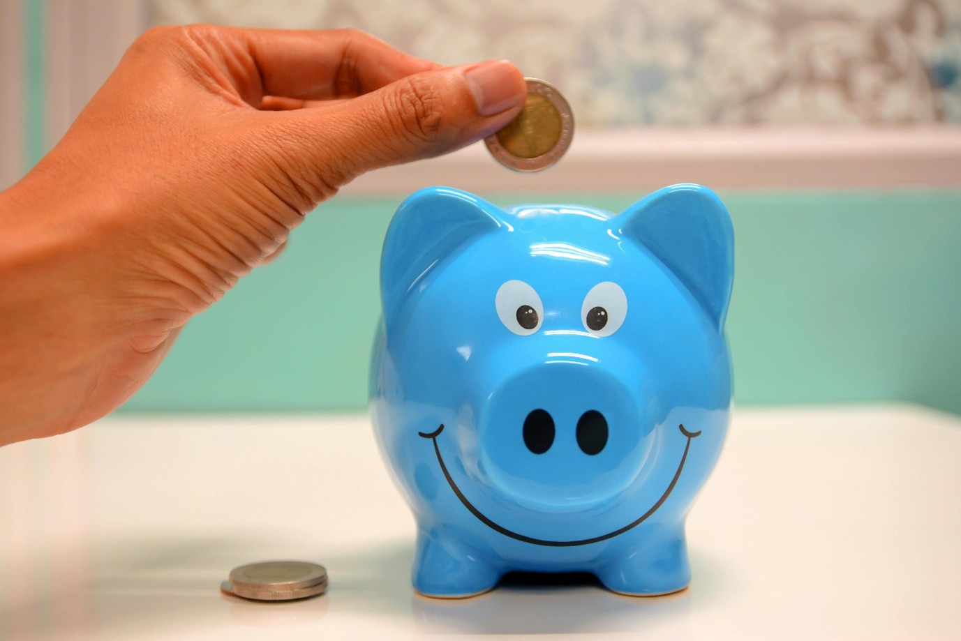Person putting a coin in a blue piggy bank